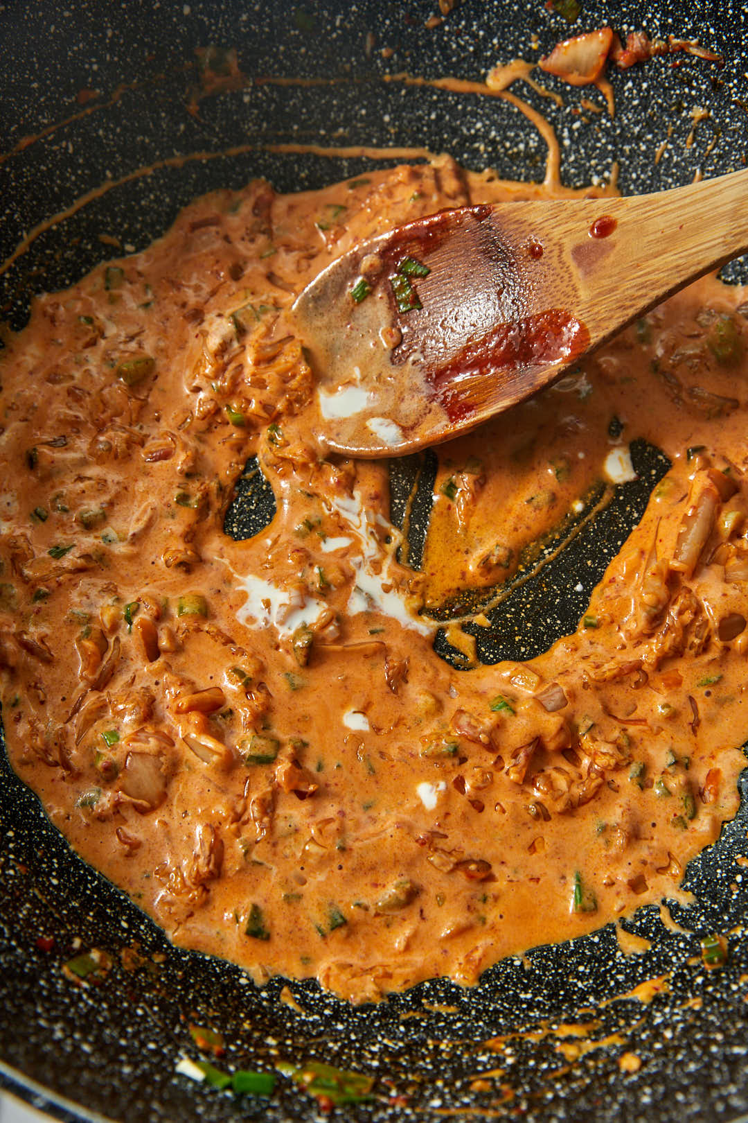 creamy kimchi sauce in a large black skillet with a wooden spoon.