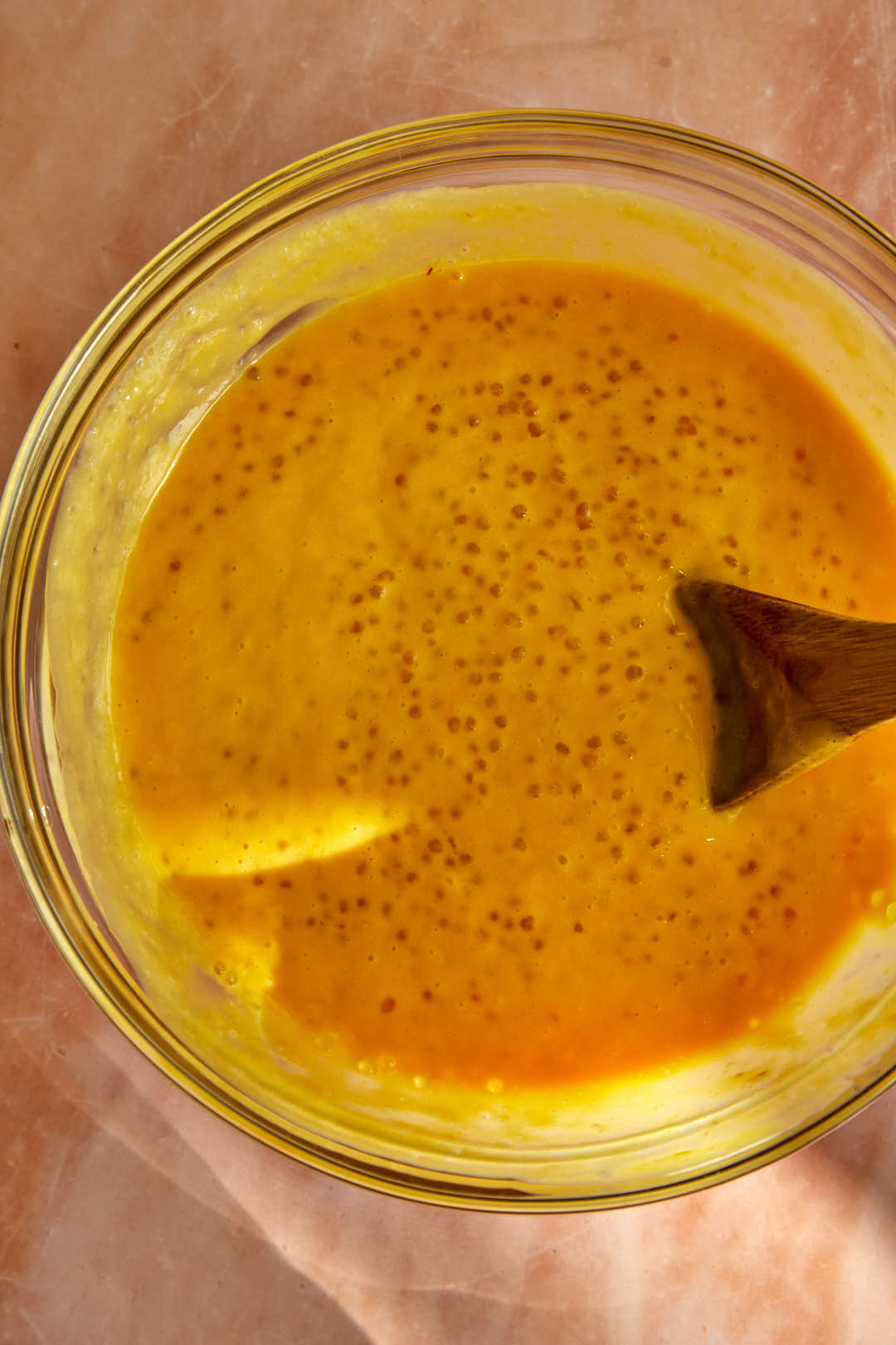 Creamy mango sago mix in a glass bowl with a wooden spoon.