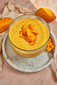 photo of mango sago in clear trifle dish on a marble plate with ripe mangoes in the background.