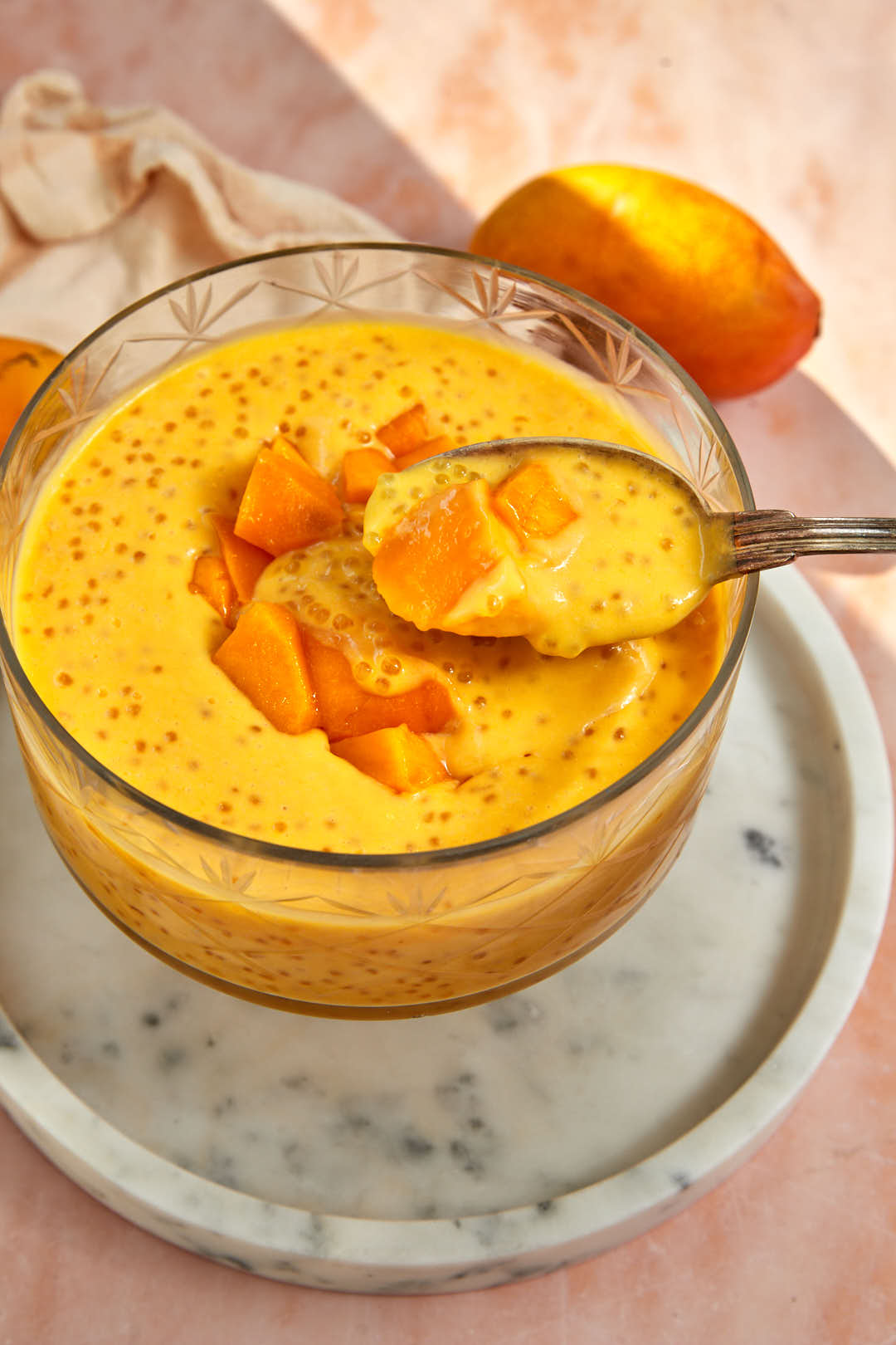 spoon scooping mango sago out of a glass dish.