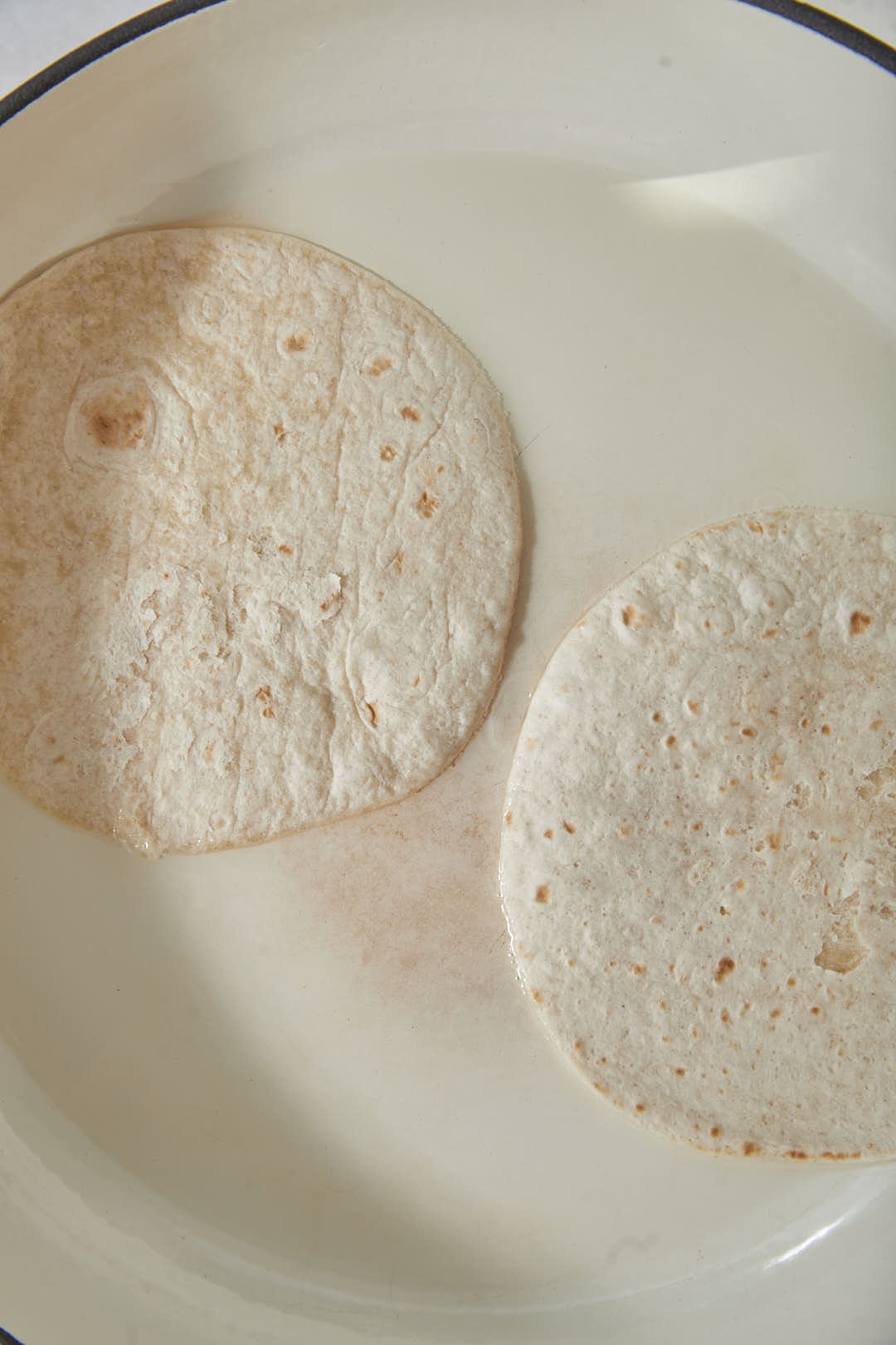 two tortillas being heated in a skillet.