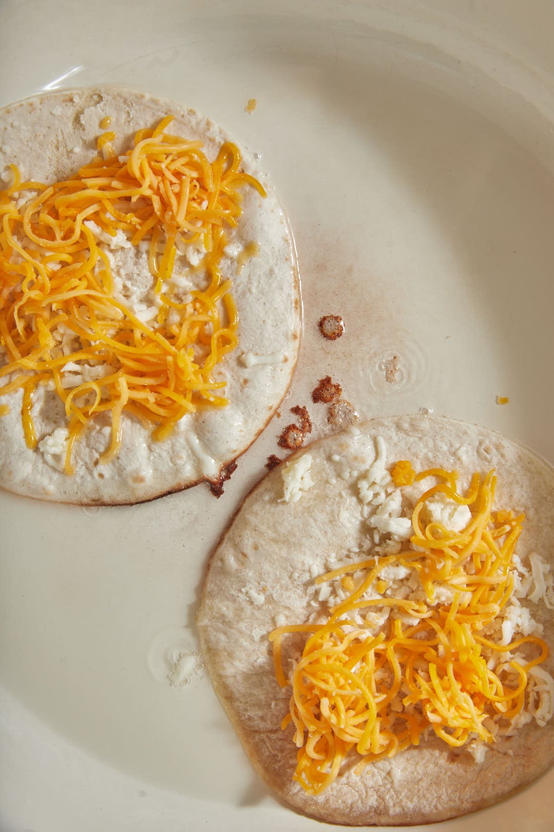 shredded cheddar cheese and mozzarella cheese on top of two tortillas in a skillet.