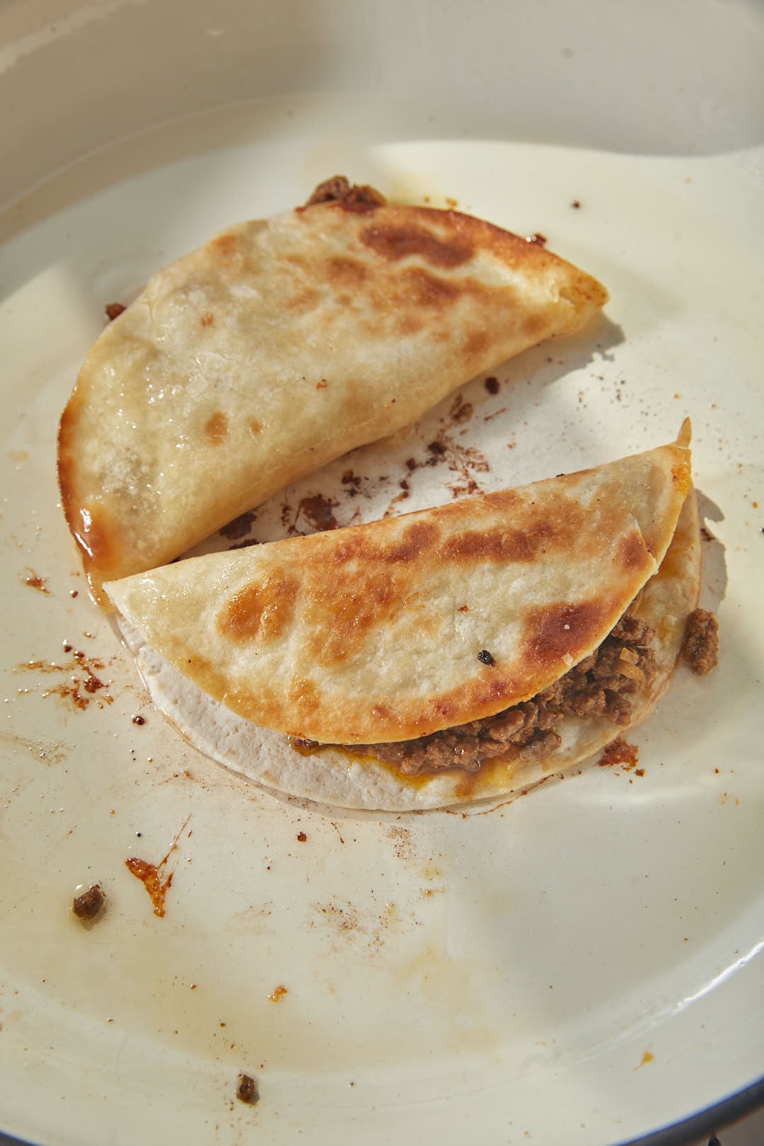 two crispy flour tortillas being heated in a large skillet.