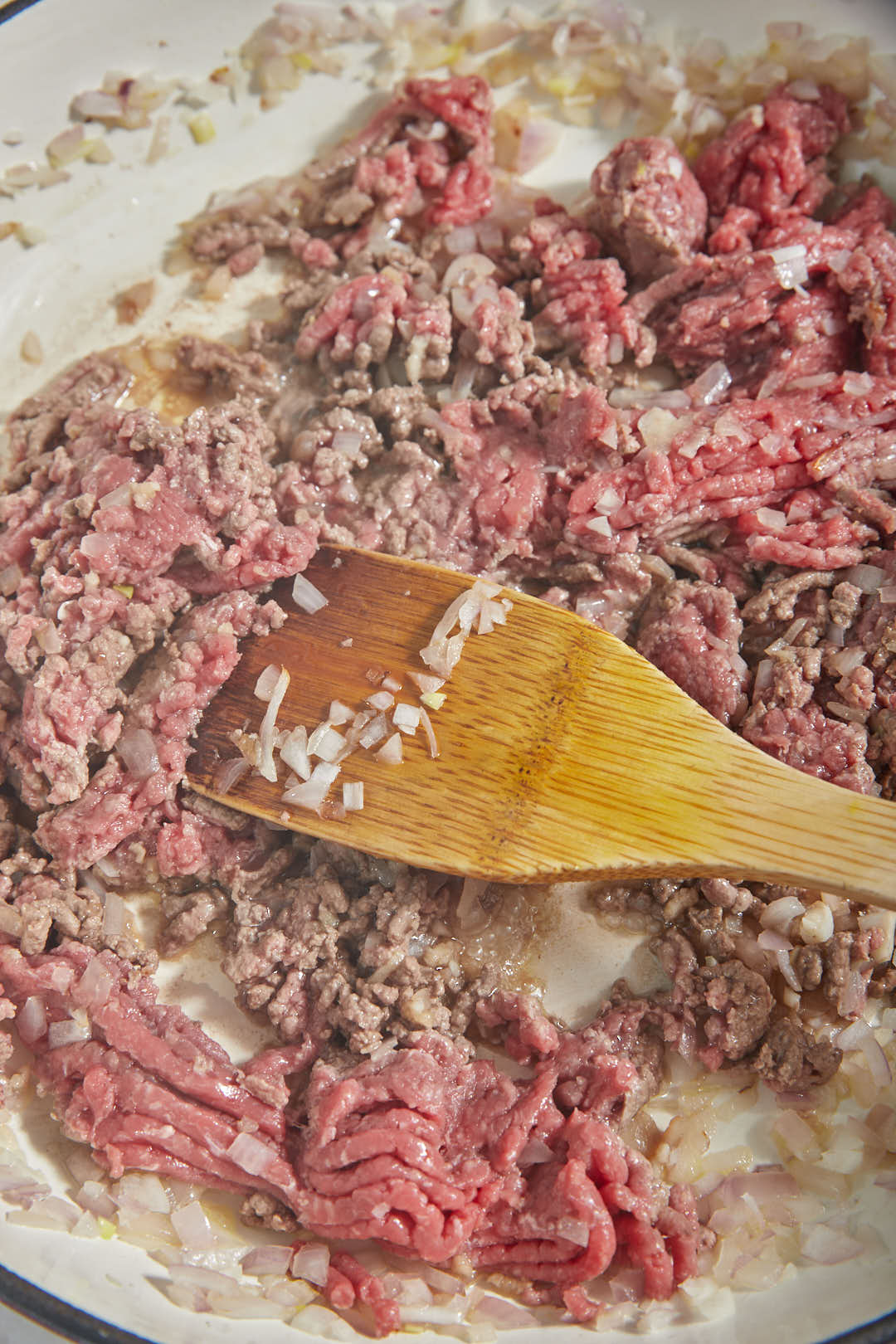 ground beef added to softened onions in a large skillet with a wooden spoon.