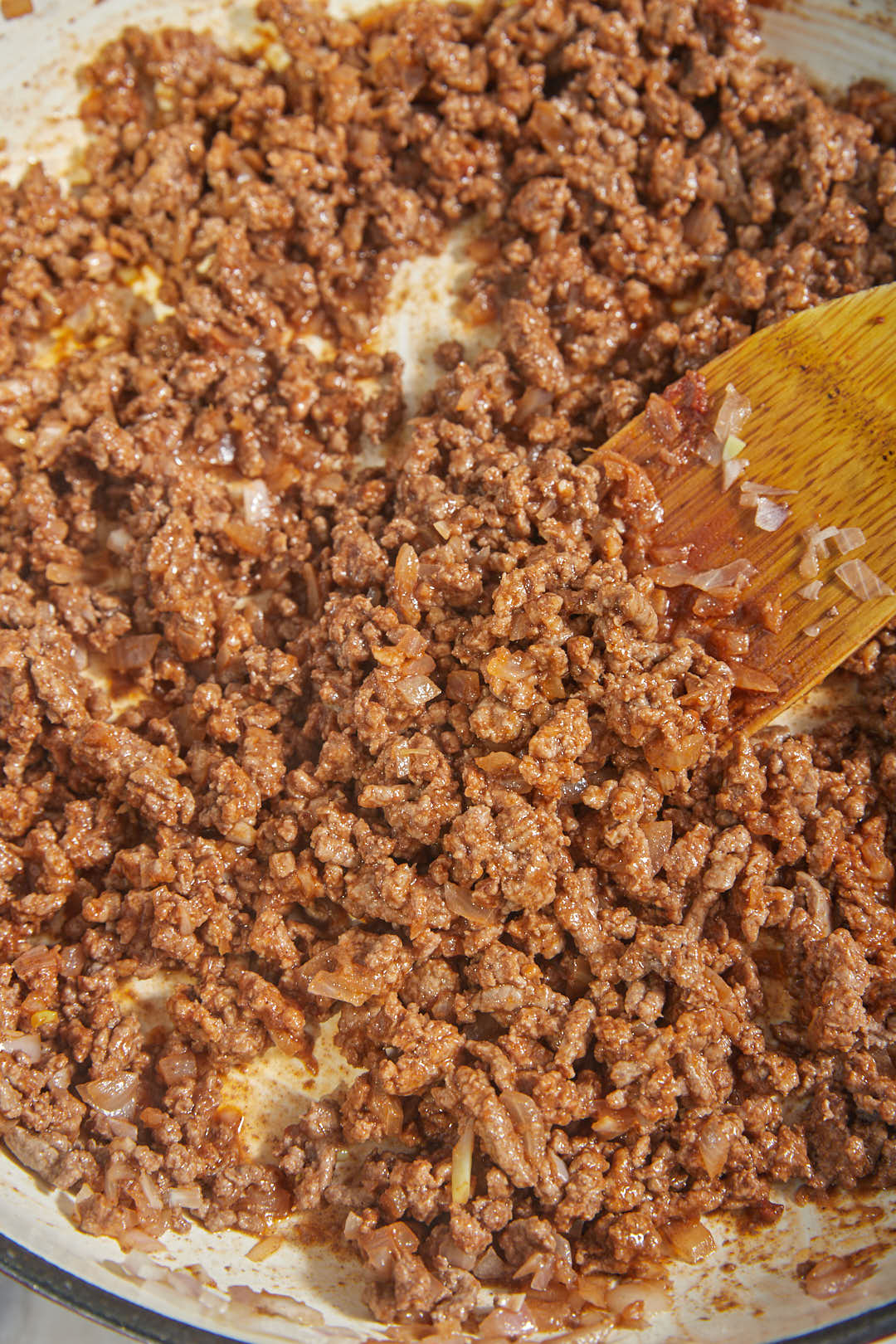 saucy taco meat in a skillet with a wooden spoon.