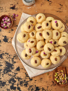 a plate of ghraybeh on a wooden background with some rose petal sin the back.