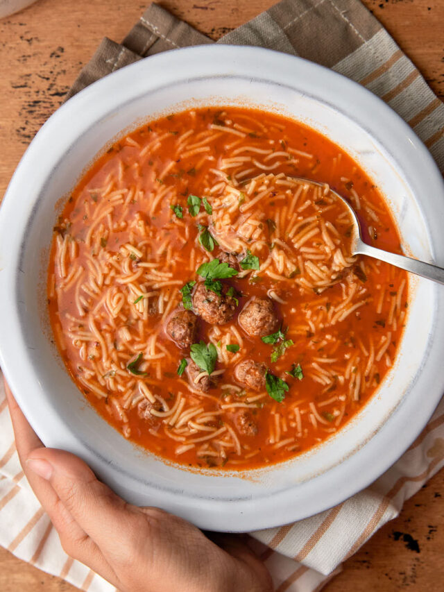 hand holding a bowl of mini meatball and noodle soup.