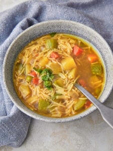 Bowl of vegetable noodle soup with a spoon taking some out.