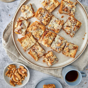 a plate of date coconut squares with a cup of coffee and some walnuts on the side.