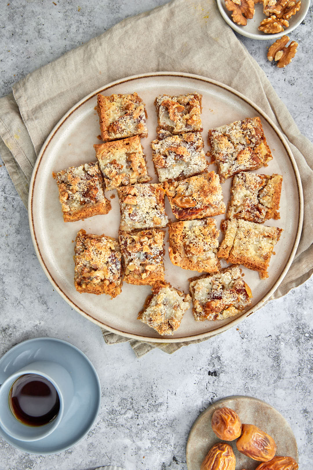 date bars cut into squares on a plate with coffee and extra dates in the background.
