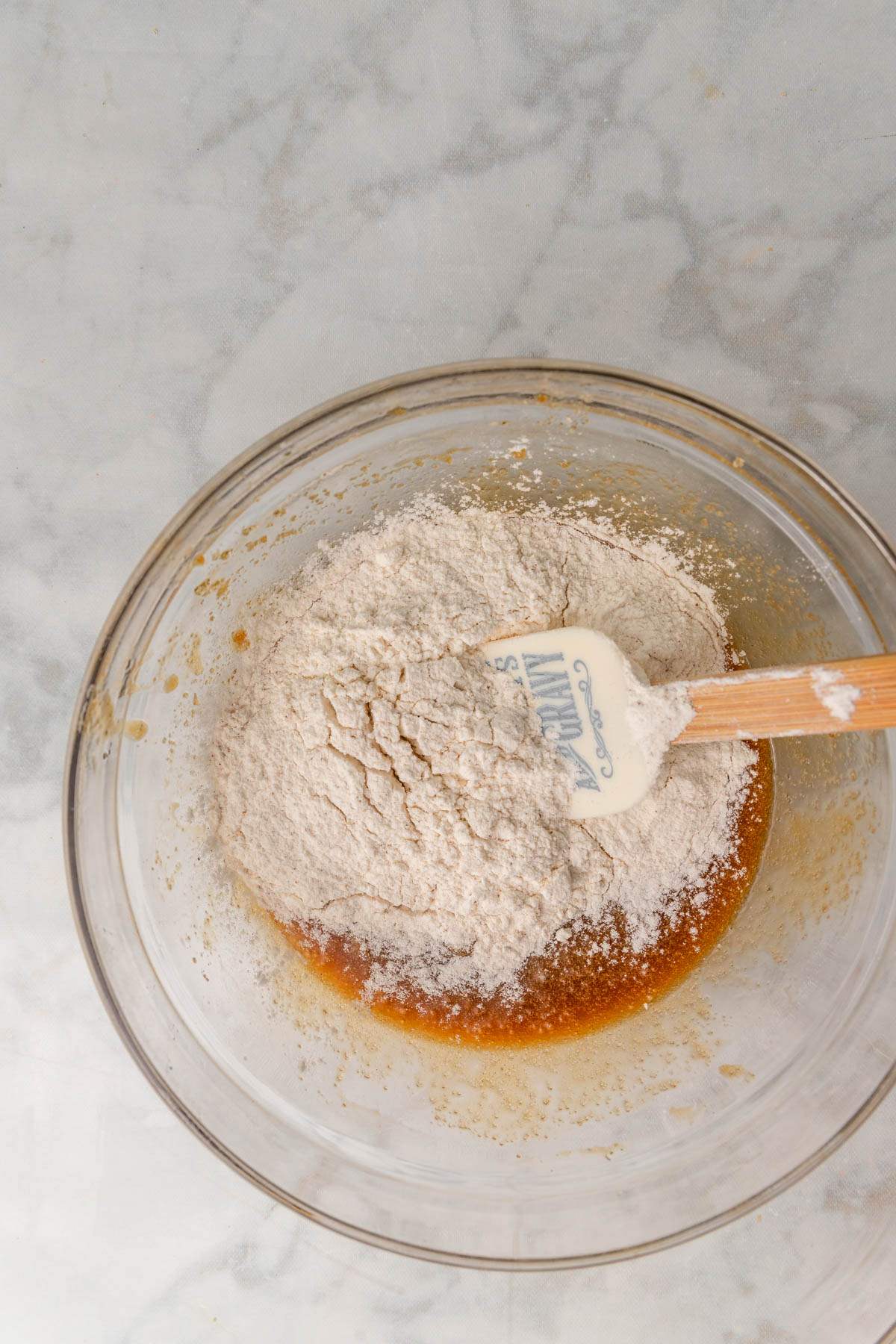 flour added to wet ingredients in a glass bowl.