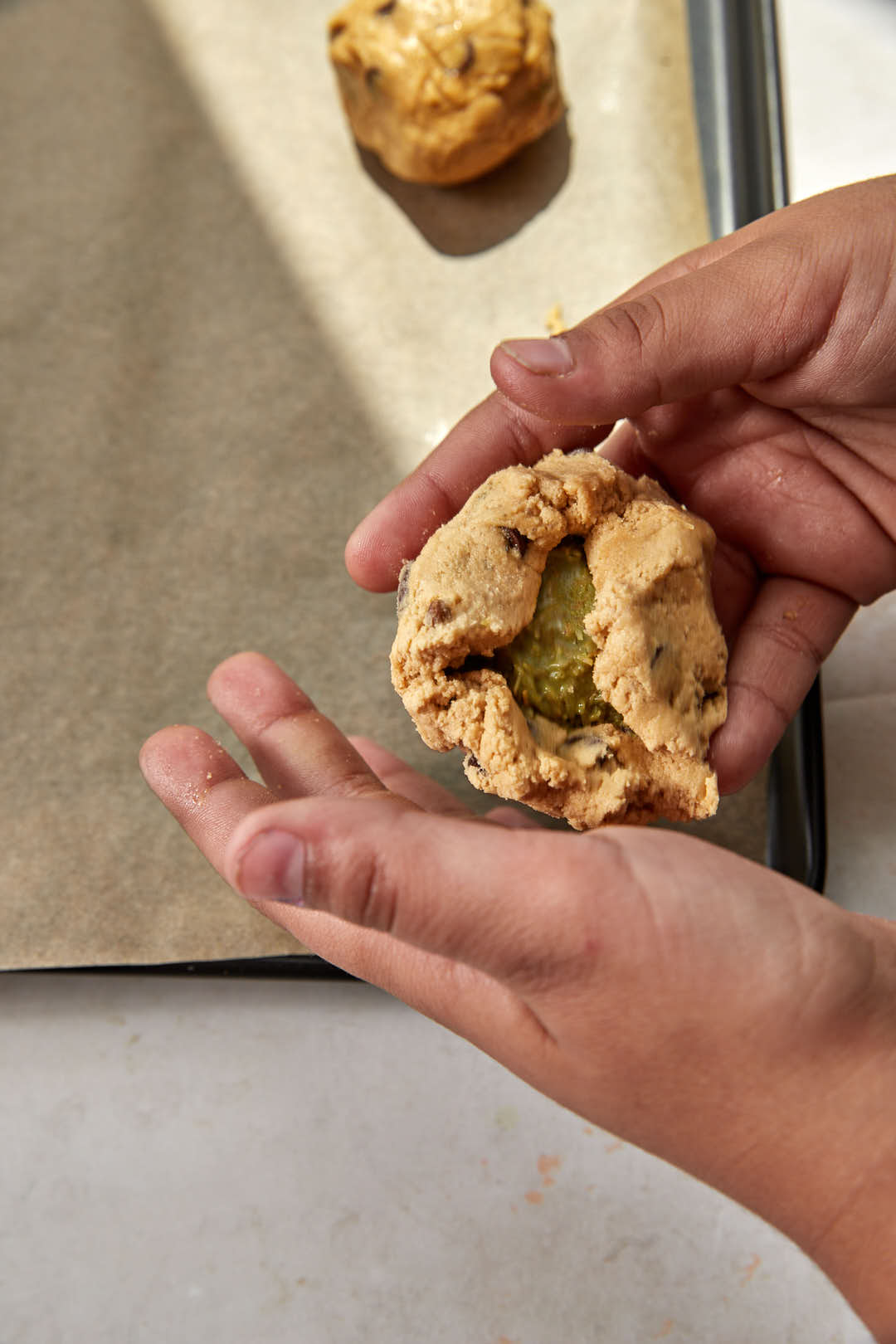 pistachio kunafa filling being stuffed inside a chocolate chip cookie dough ball.