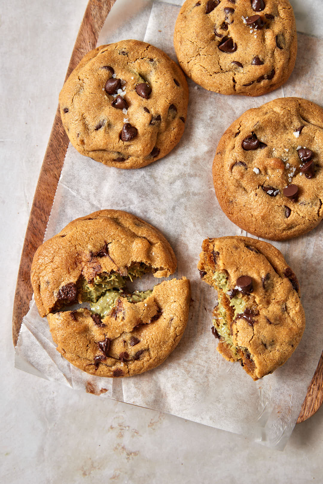 dubai chocolate chip cookies broken in half on a parchment paper lined wooden board.