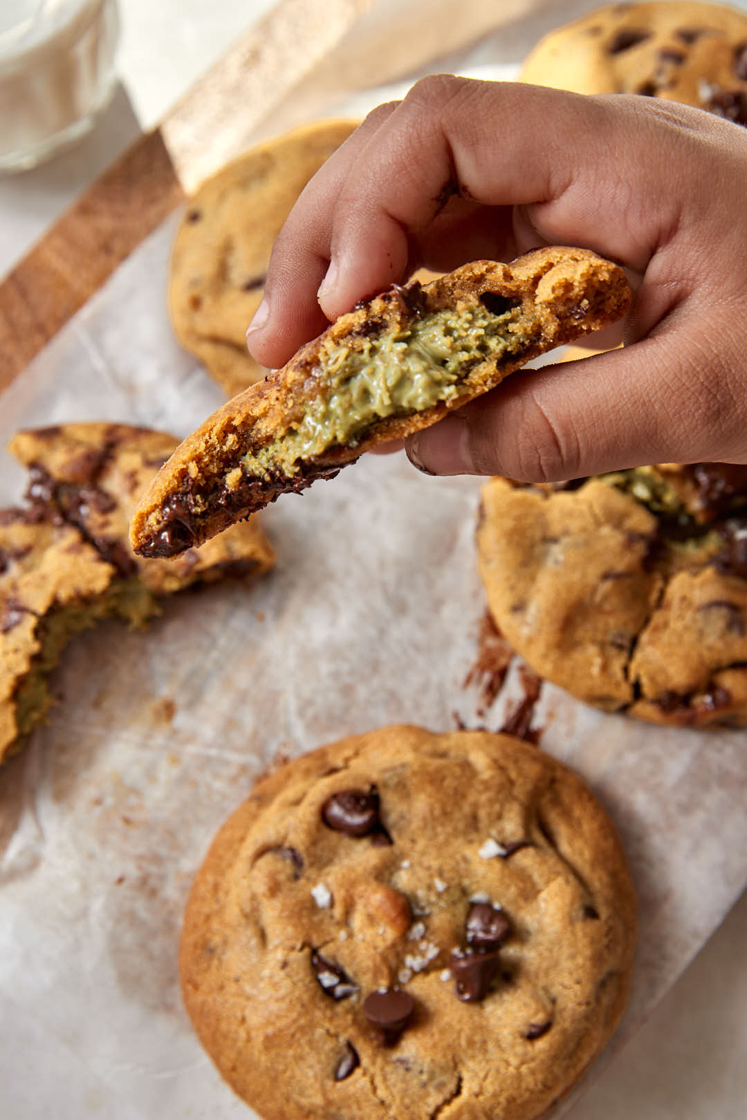 A child's hand holding a dubai chocolate cookie with a bite taken out and the pistachio kunafa filling exposed.