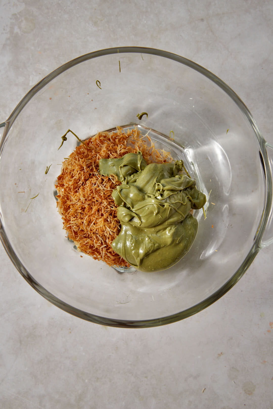 Pistachio cream added to toasted kunafa in a glass bowl.