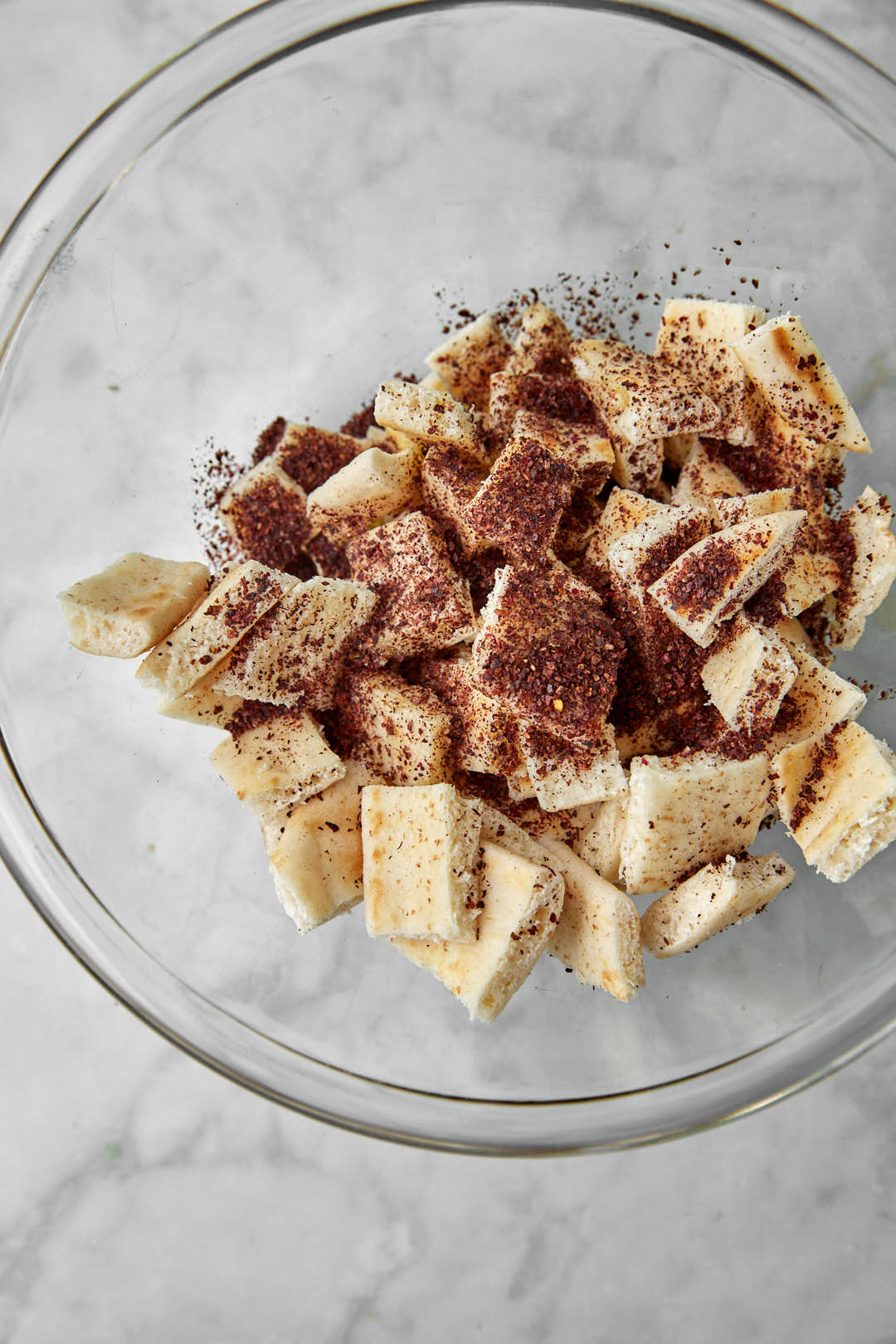 pita bread cut into cubes with sumac powder in a glass bowl.