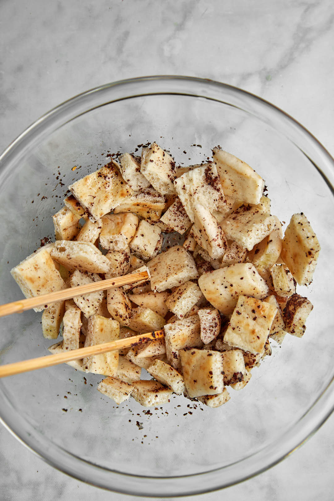 pita bread cubes tossed with olive oil and sumac in a glass bowl.