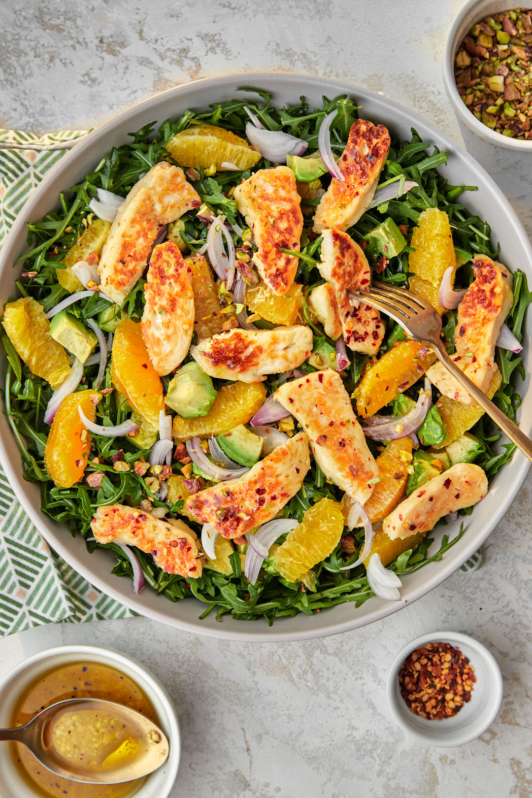 a big gray serving platter with fried halloumi salad with orange, avocado and pistachios, and a fork spearing one slice of halloumi.