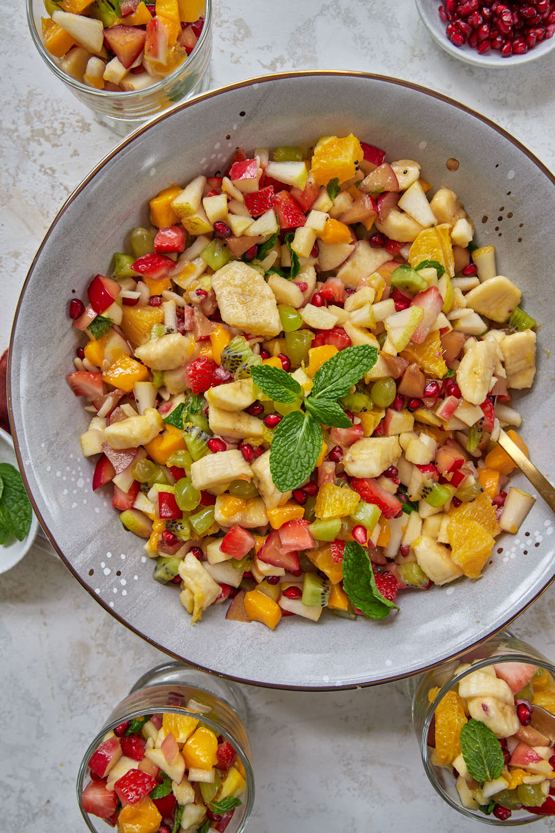 lebanese fruit salad with citrus dressing in large gray bowl, with small portions of fruit salad surrounding it.