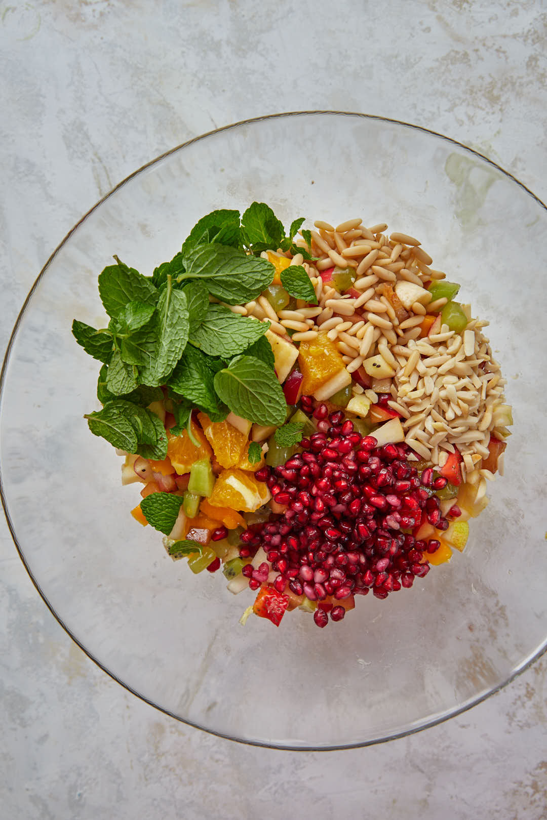 pomegranate seeds, nuts, and mint leaves on top of the fruit salad in a bowl.