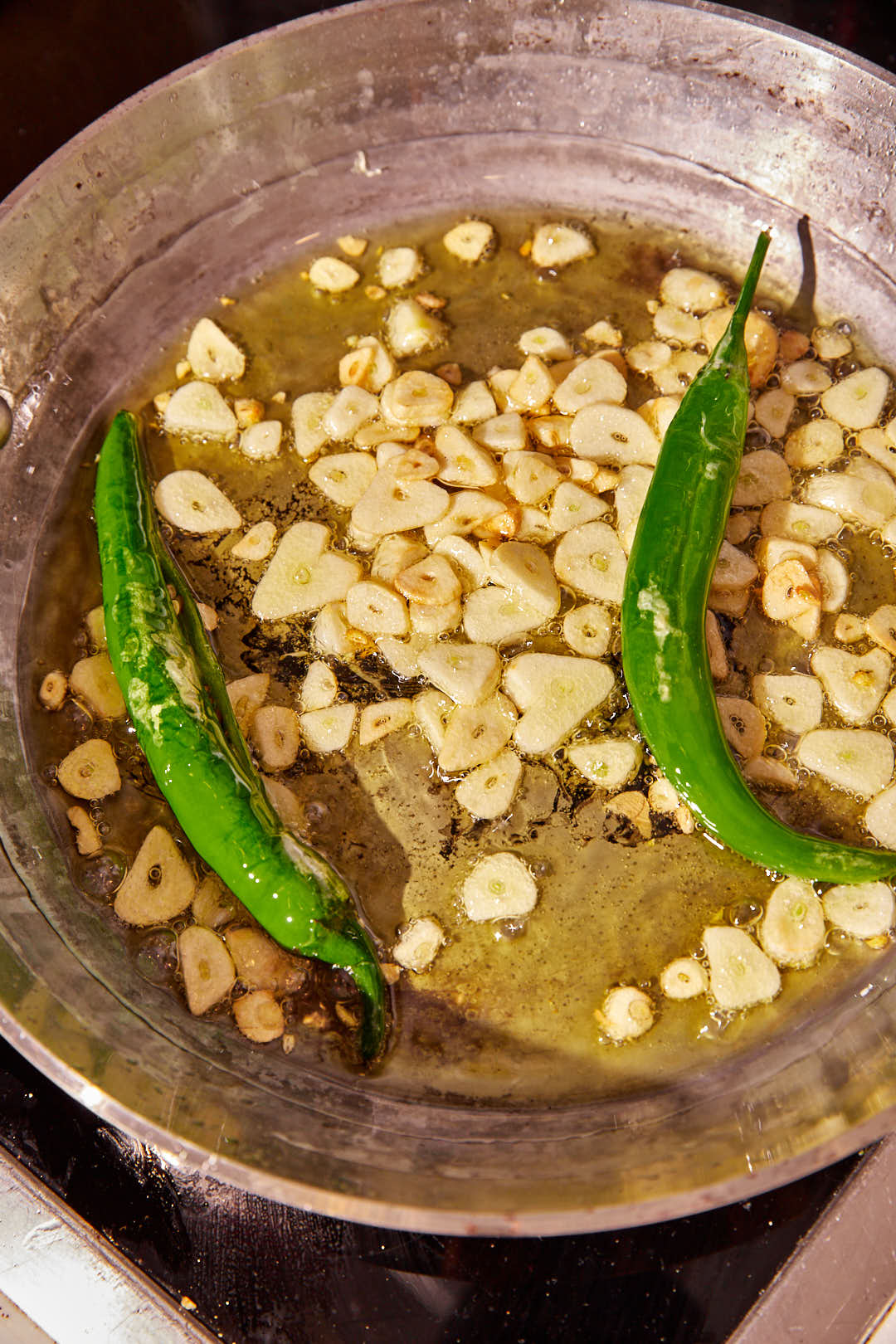 sliced garlic and green chili peppers sizzling in hot oil.
