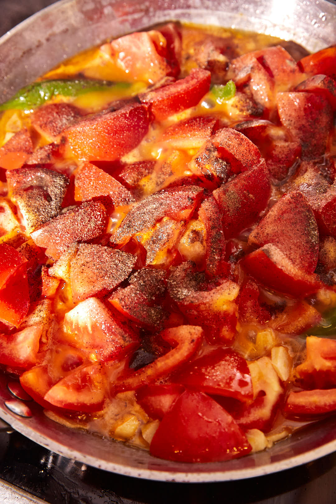 salt and black pepper added to tomato cubes and green chili peppers in a skillet.