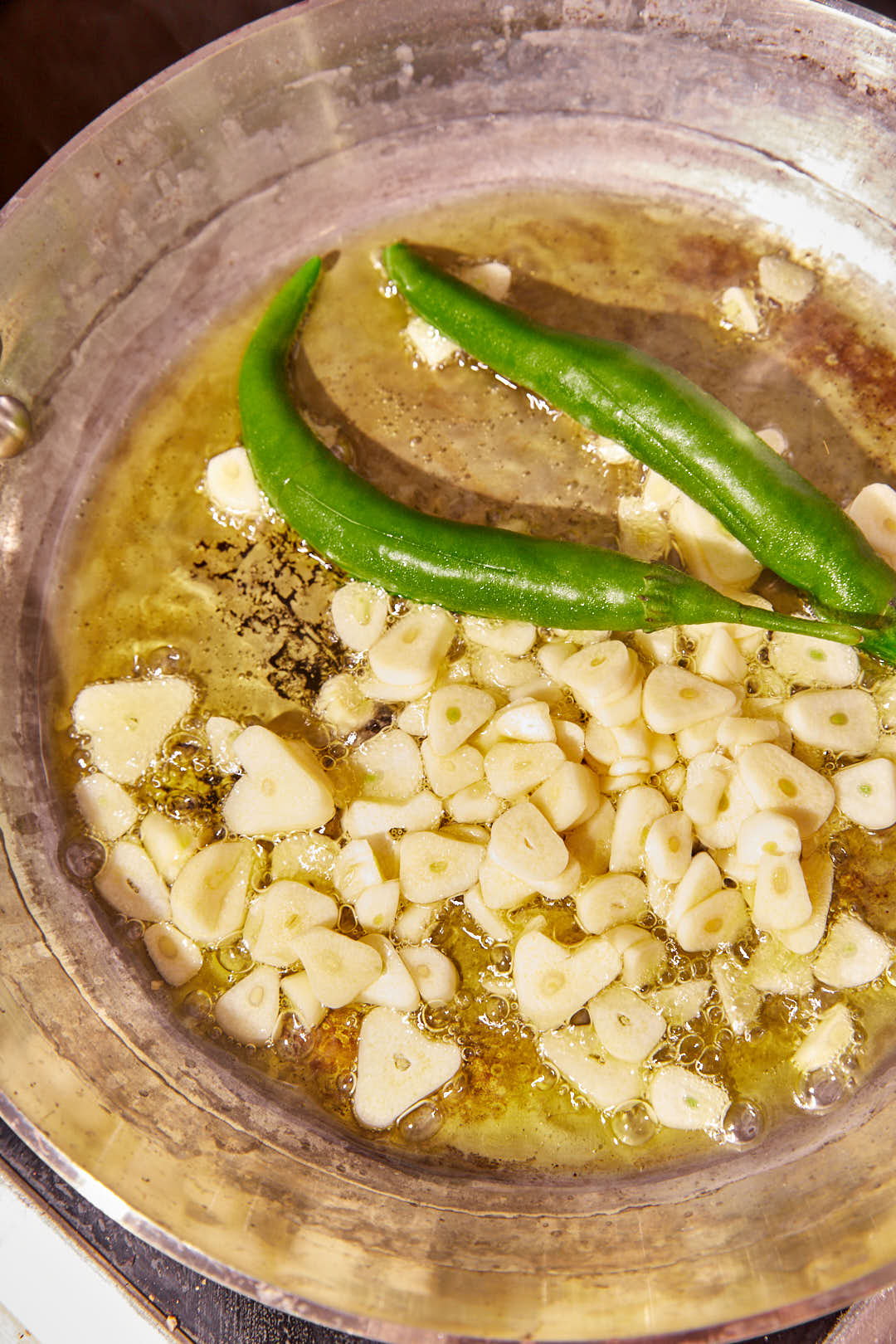 lots of sliced garlic and two green chili peppers in olive oil in a skillet.