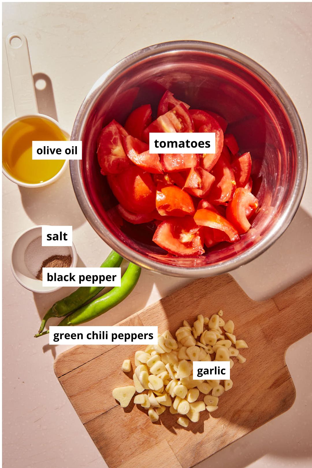 ingredients needed to make galayet bandora- tomatoes, chilis, garlic, olive oil, salt and black pepper, on a warm marble background.
