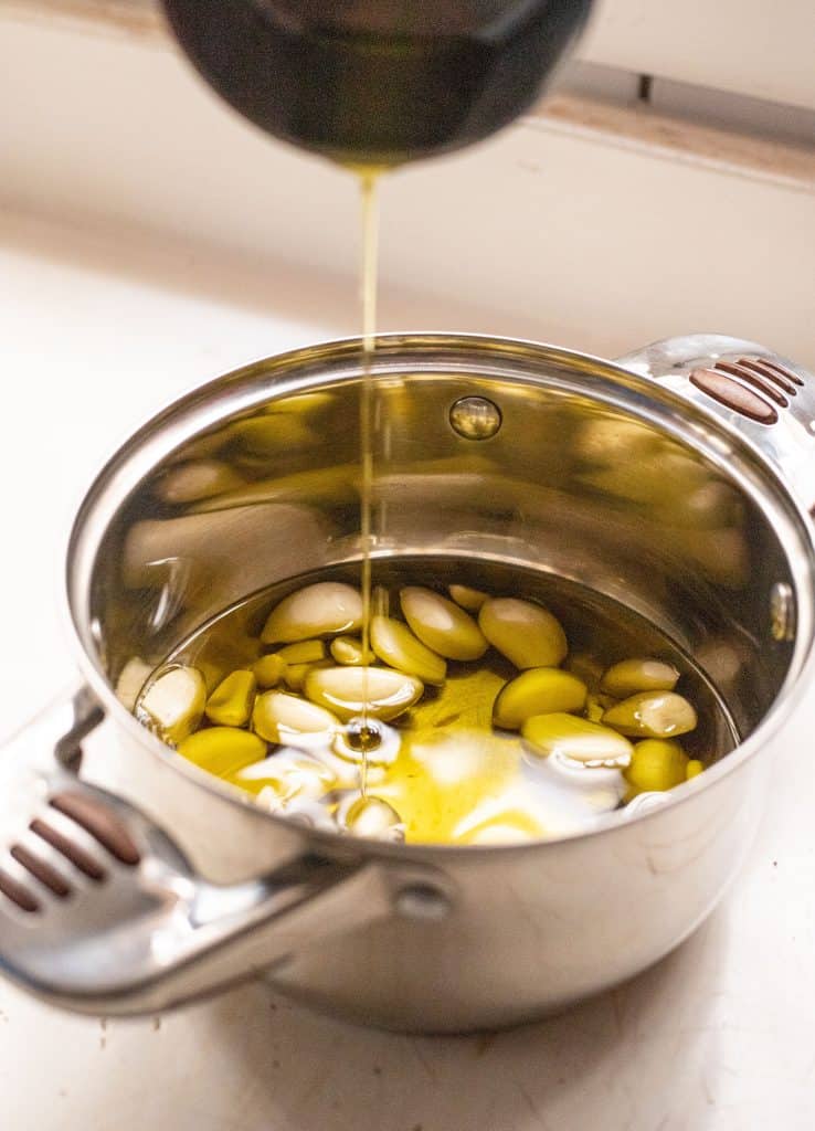 Adding olive oil to a saucepan full of garlic cloves