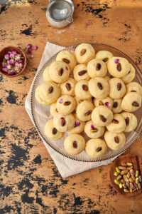 a plate of ghraybeh on a wooden background with some rose petal sin the back.