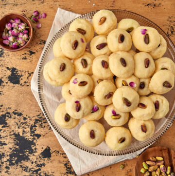 a plate of ghraybeh on a wooden background with some rose petal sin the back.