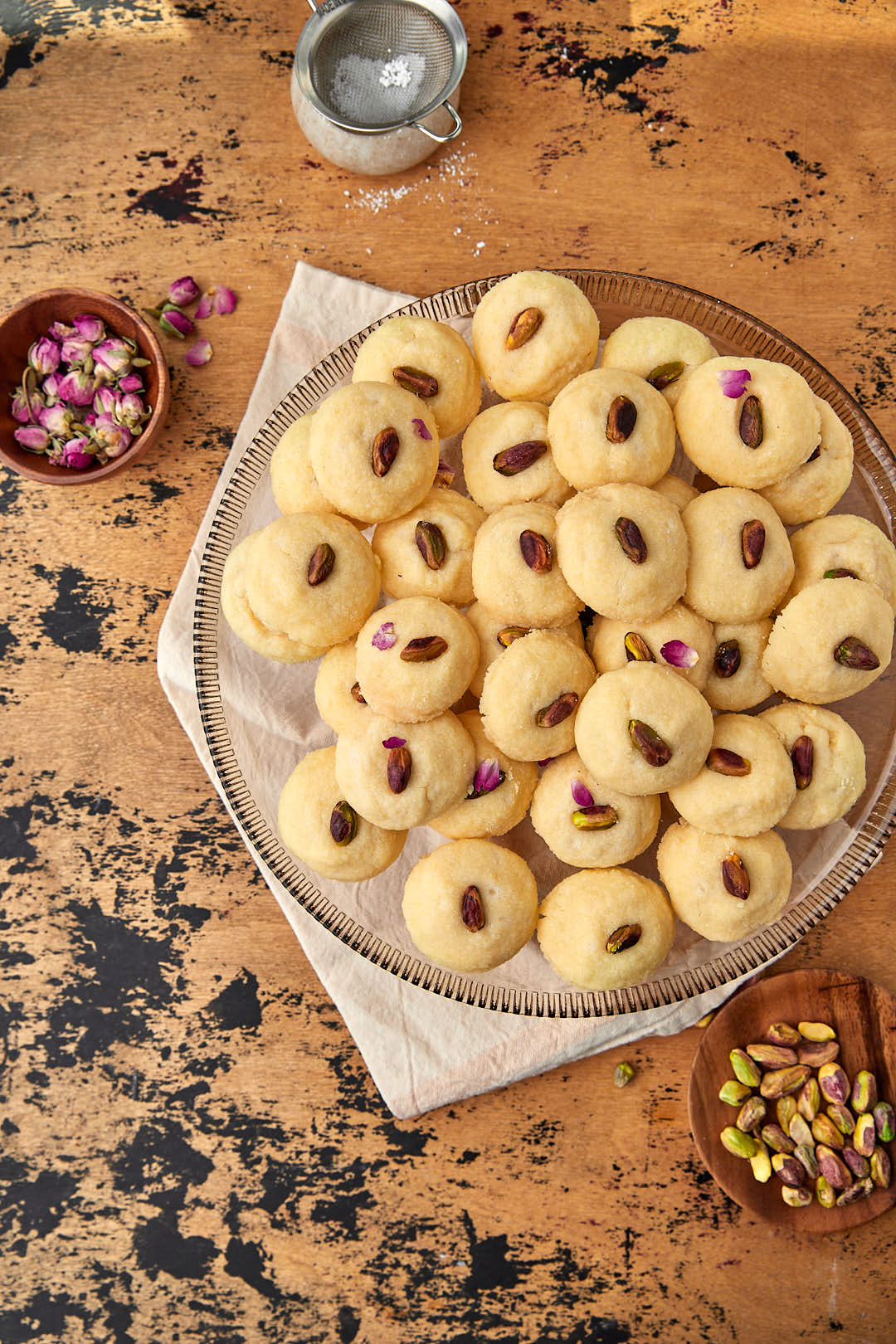 a plate of ghraybeh on a wooden background with some rose petal sin the back.