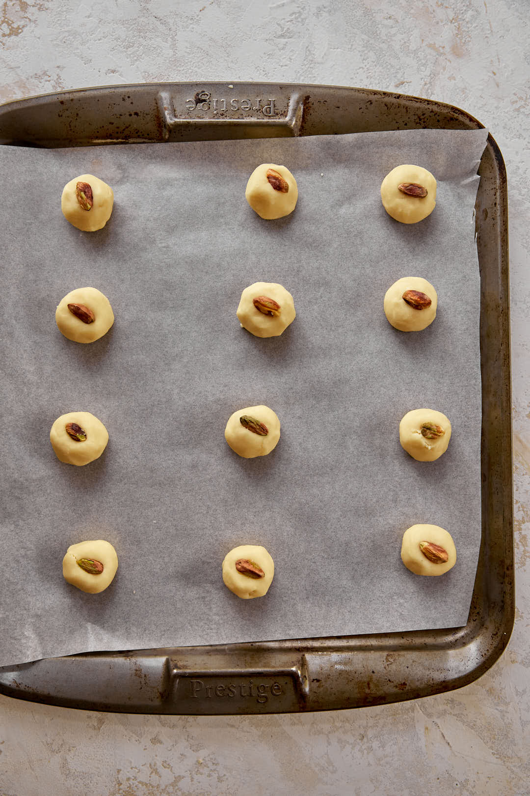 pistachio slivers pressed onto dough balls in baking tray.