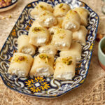 platter of halawet el jibn on a lacey tablecloth with sugar syrup in the background.