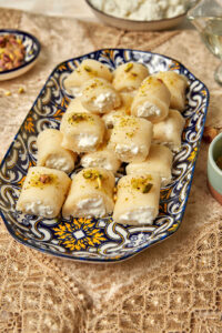 platter of halawet el jibn on a lacey tablecloth with sugar syrup in the background.
