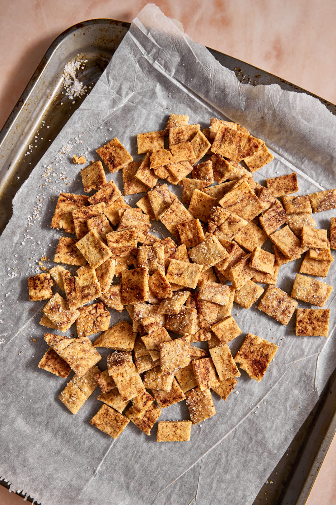 a baking sheet lined with parchment paper with baked cinnamon toast crunch piled in the center.