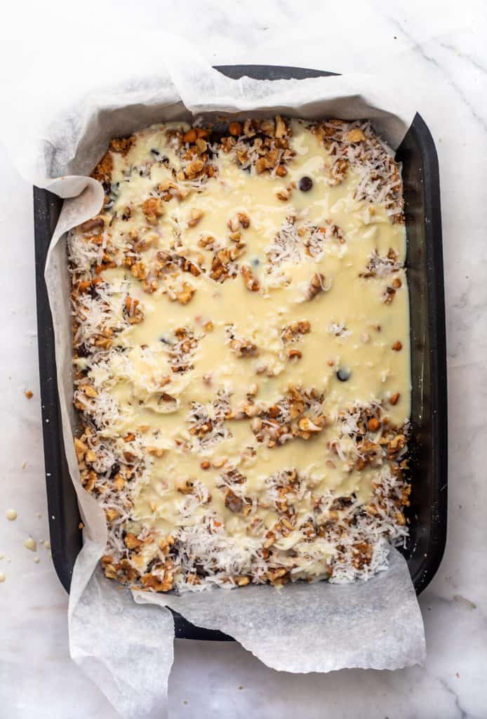 seven layer bars in pan with condensed milk drizzled on them before baking
