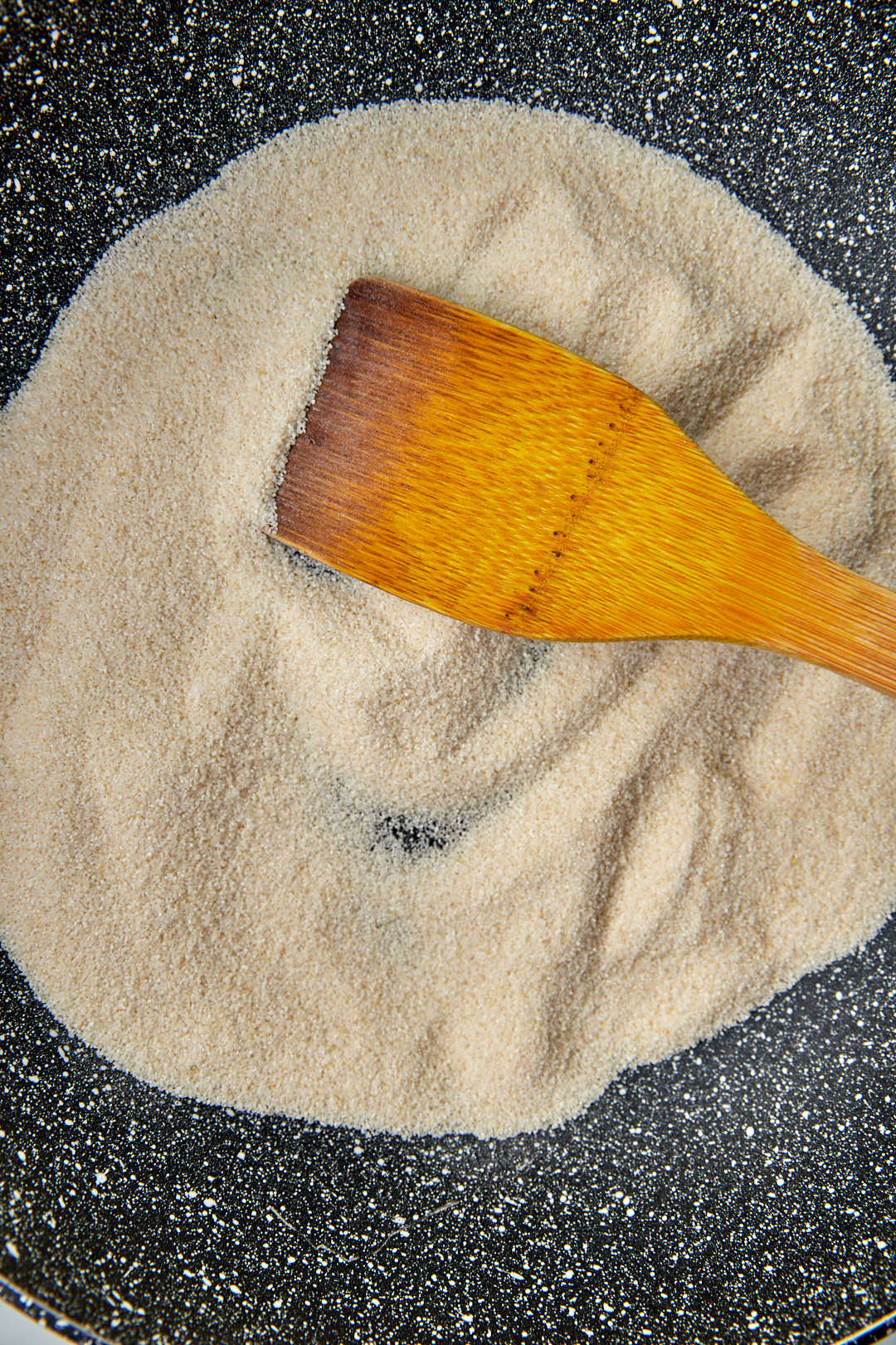 semolina powder in a skillet with a wooden spatula.