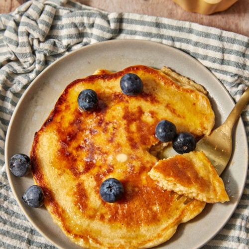 a large cottage cheese pancake with blueberries scattered on top, on a blue and white striped linen towel