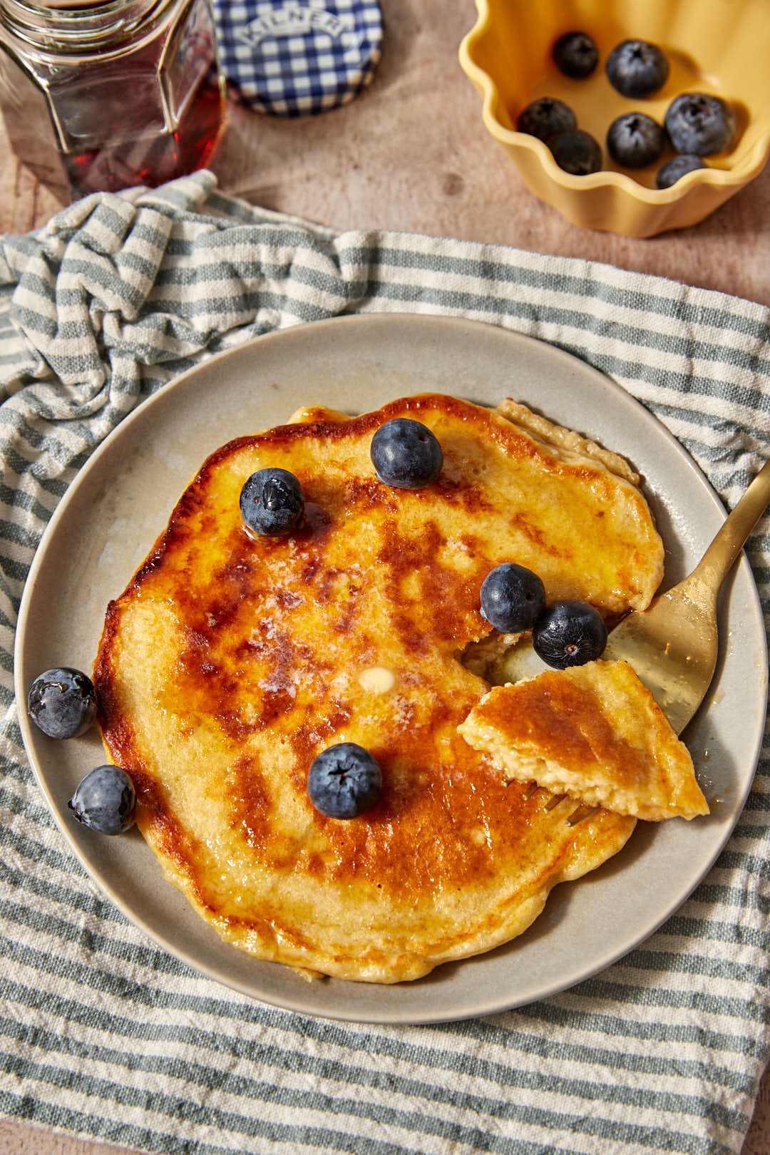 a large cottage cheese pancake with blueberries scattered on top, on a blue and white striped linen towel
