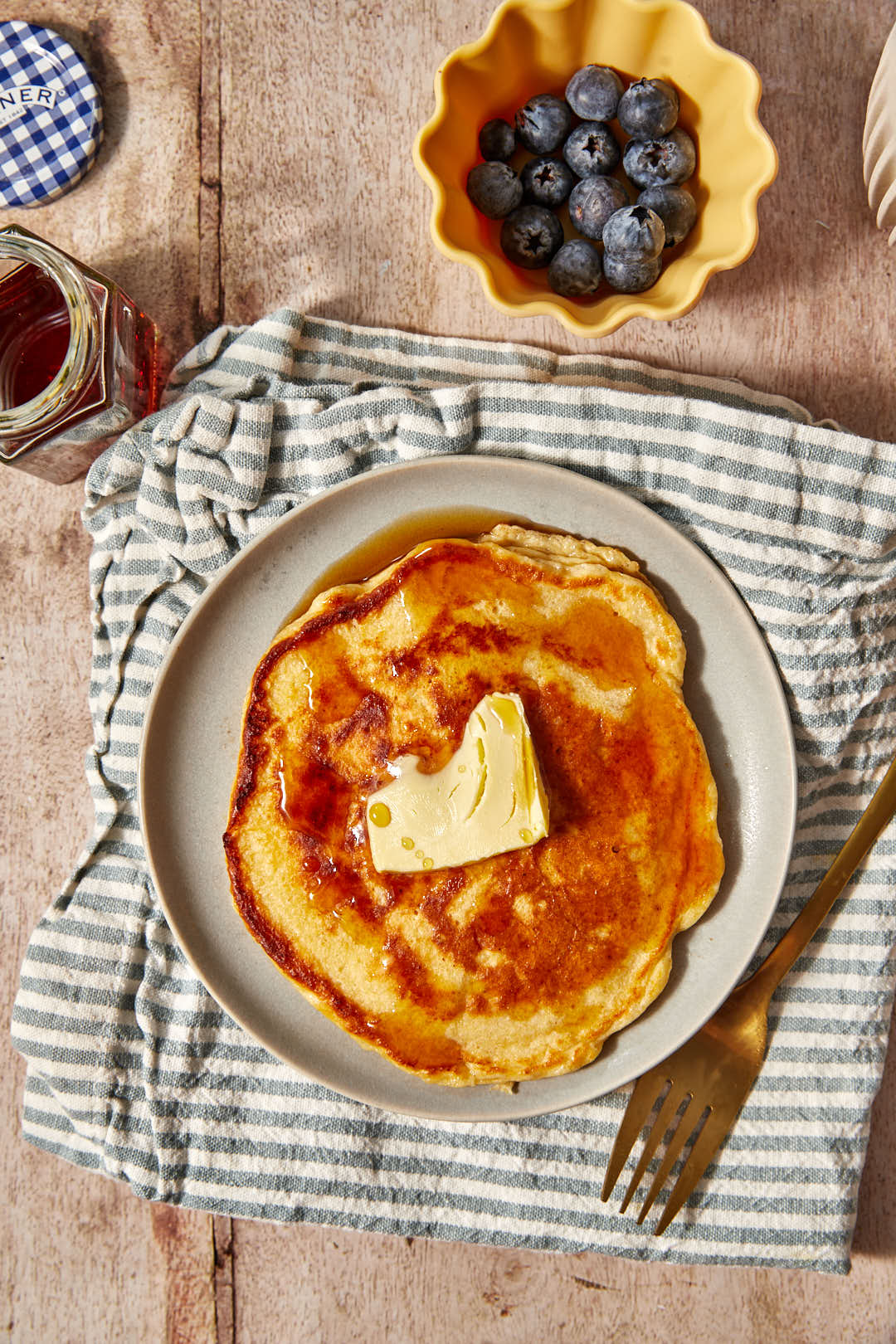 pancake on a blue and white striped kitchen towel with a small bowl of blueberries in the background.