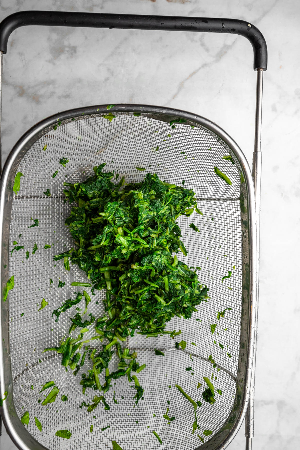 chopped dandelion greens being washed and strained over colander.