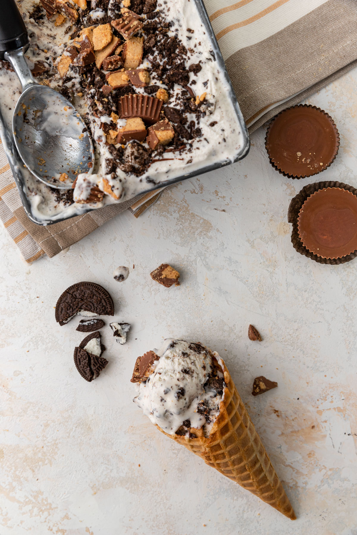 ice cream cone with oreo ice cream with broken oreo and reese's pieces on background.