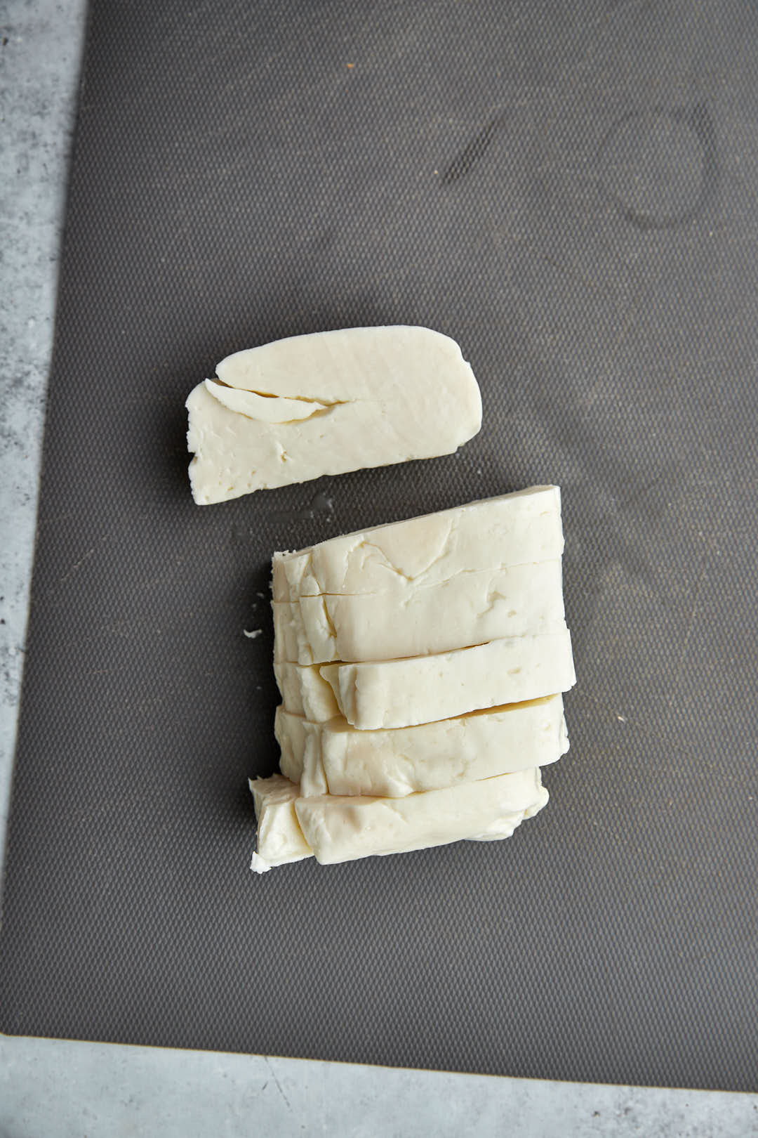 halloumi block being sliced on a gray cutting board.