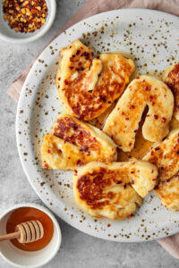 a close up photo of sliced grilled halloumi in a hot honey sauce on a white plate.