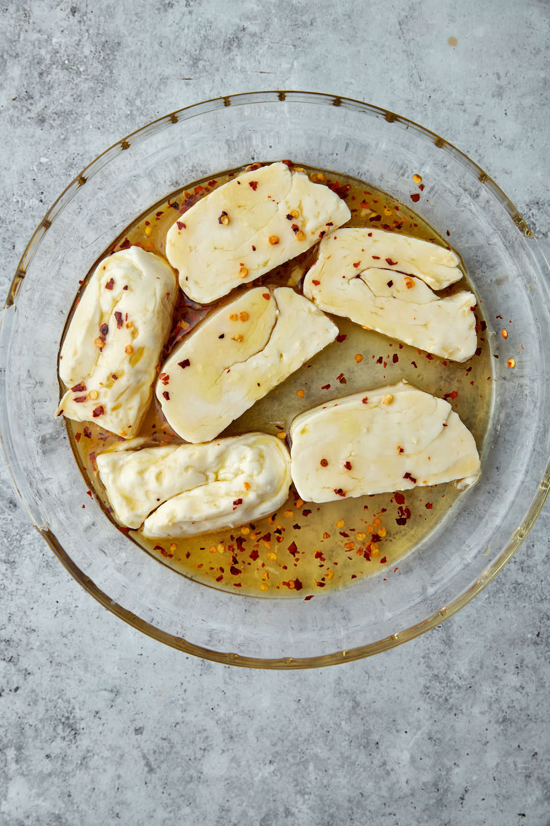 halloumi slices marinating in hot honey sauce in glass bowl.