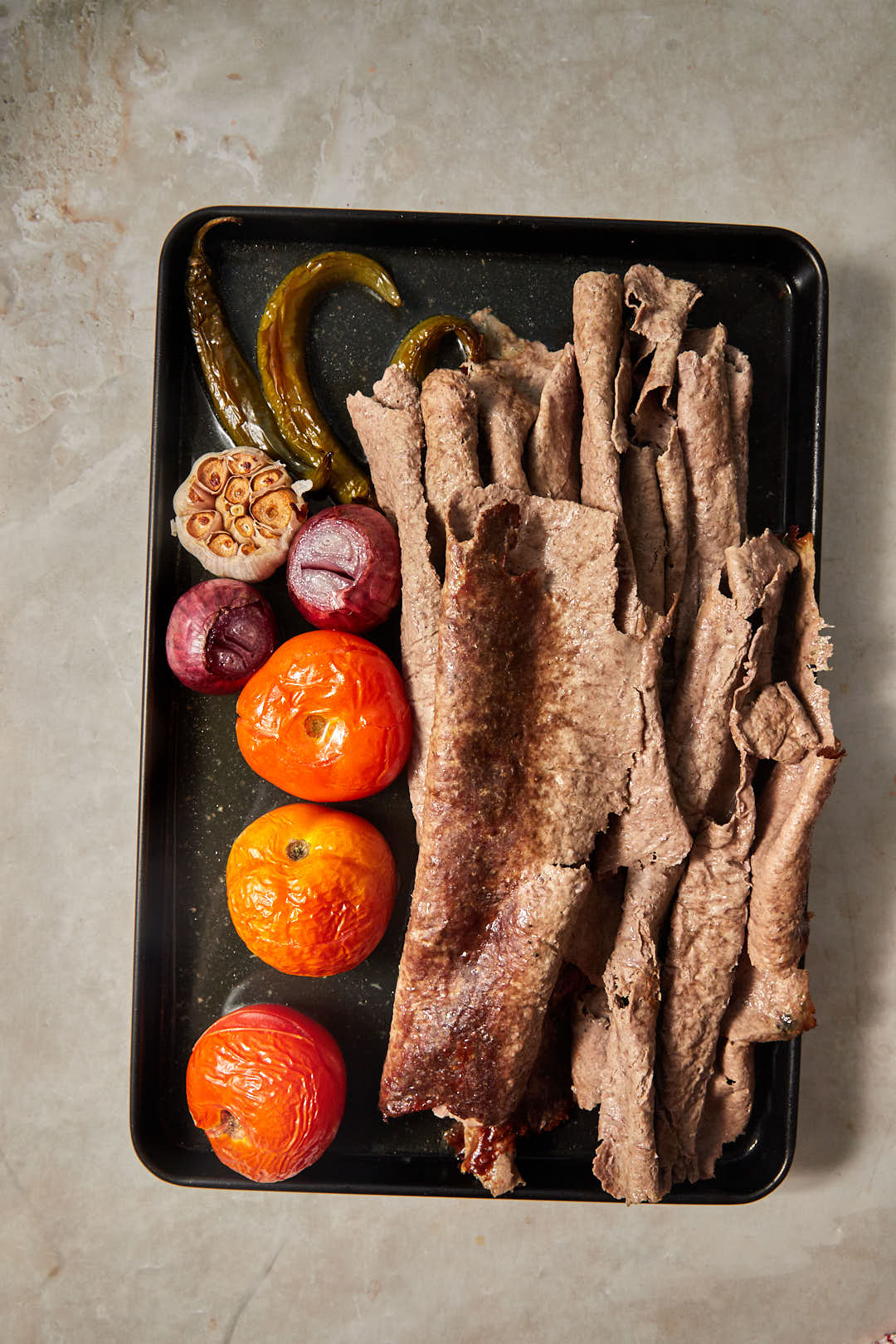 cooked doner kebab meat on a baking sheet with roasted vegetables.