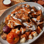 A plate of homemade iskender kebab with sauce on the side.
