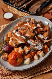 A plate of homemade iskender kebab with sauce on the side.