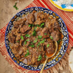 photo of kebab halla on a colorful plate with rice on another plate in the background.